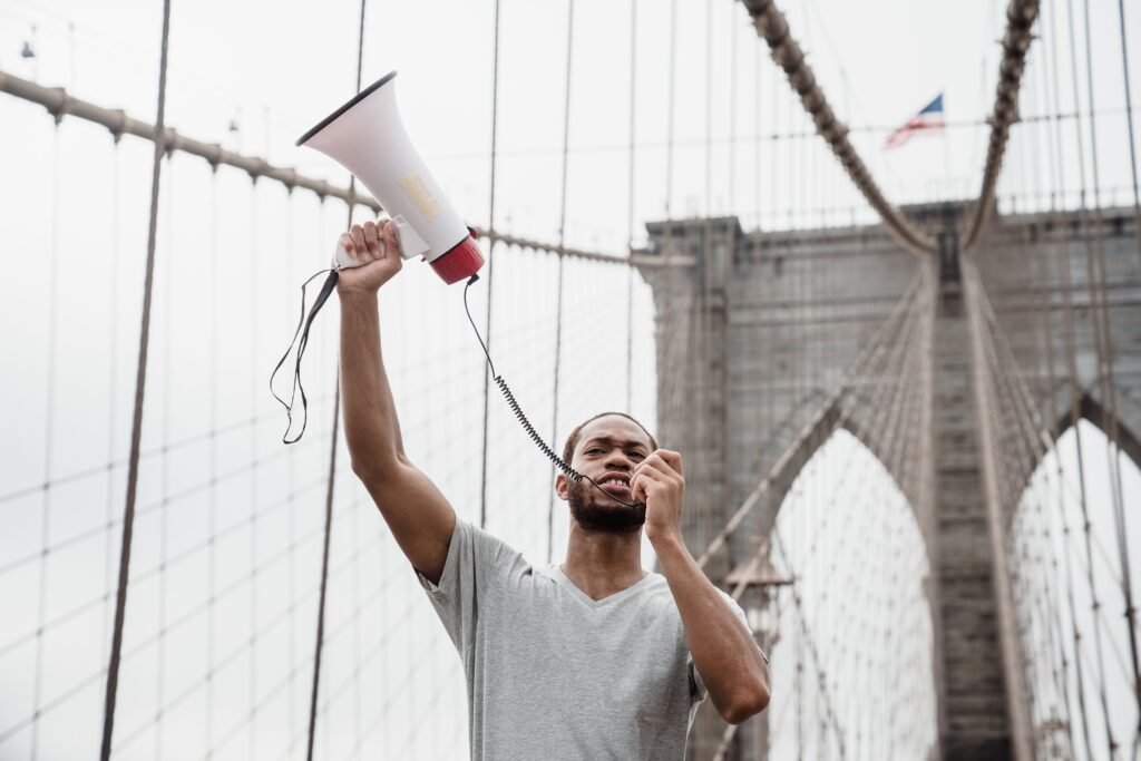 Person standing on Brooklyn Bridge holding a megaphone, symbolizing protest.